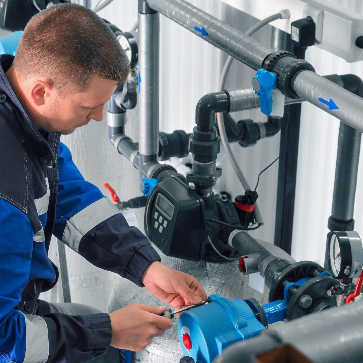 Man checks pipes in production room. Plumber is repairing water supply system. Man checks pipes in production room. Plumber is repairing water supply system. Middle-aged Caucasian worker in overalls works in boiler room.