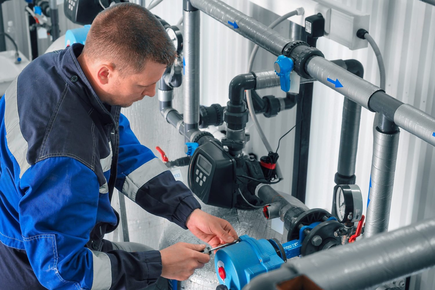 Man checks pipes in production room. Plumber is repairing water supply system. Man checks pipes in production room. Plumber is repairing water supply system. Middle-aged Caucasian worker in overalls works in boiler room.